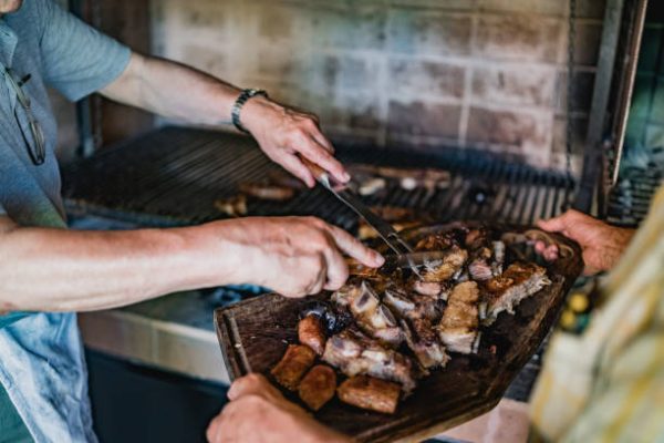 Two men cutting and serving barbecue meat at home for family.